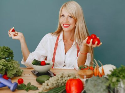 Healthy lifestyle concept with woman holding tomatoes and surrounded by fresh vegetables in a studio setting.